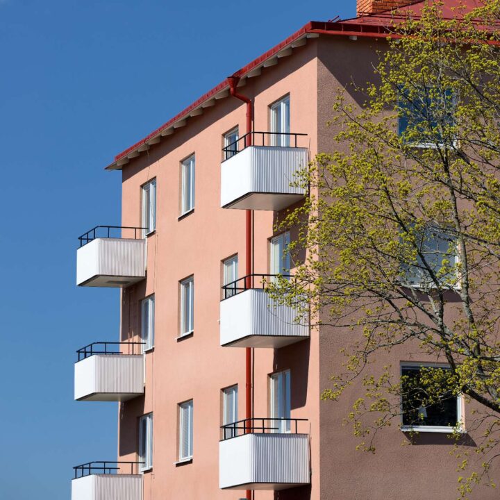 En rosa husfasad med vita balkonger och blå himmel