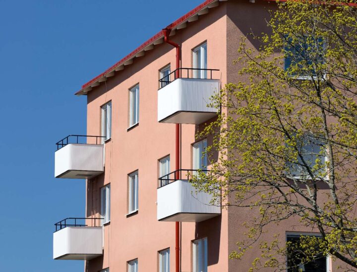 En rosa husfasad med vita balkonger och blå himmel