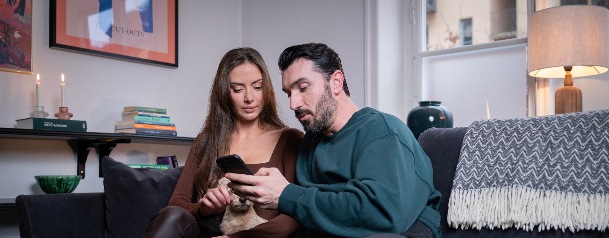 Par och hund i andrahandslägenhet tittar på mobiltelefon